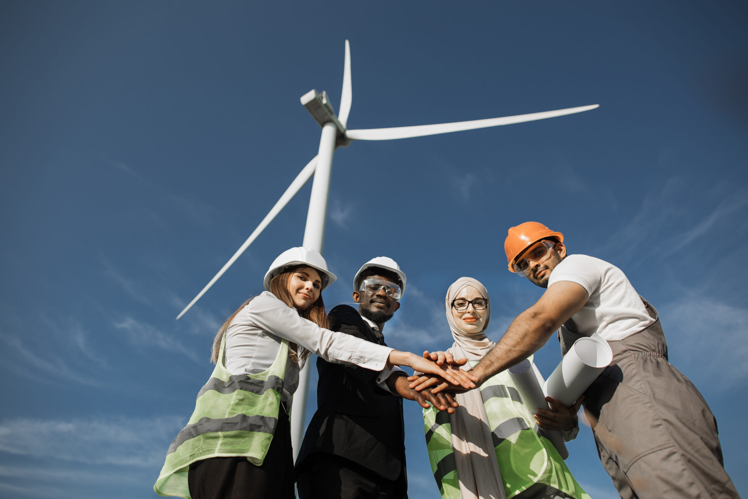 Multicultural partners stacking hands among windmill farm